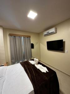 um quarto com uma cama com lençóis brancos e uma televisão de ecrã plano em Pousada Vento Solar Búzios em Búzios