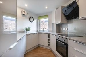 una cocina con armarios blancos y un reloj en la pared en ** Modern Merchant City 1 BED Apartment with Free Parking **, en Glasgow