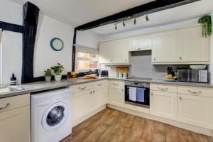cocina con armarios blancos, lavadora y secadora en Loft Cottage by Spa Town Property - 2 Bed Tudor Retreat Near to Stratford-upon-Avon, Warwick & Solihull, en Stratford-upon-Avon