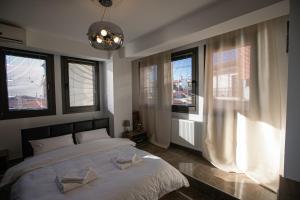 a bedroom with a bed with white sheets and windows at Stunning city view apt & parking space at Old town in Thessaloniki