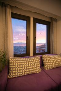Sofá púrpura con 2 almohadas frente a 2 ventanas en Stunning city view apt & parking space at Old town en Tesalónica