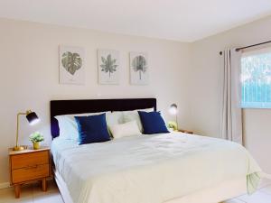 a white bedroom with a large bed with blue pillows at Coco Palms Apartments By Lowkl in Lighthouse Point