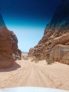 a dirt road in a desert with a rocky cliff at Qais Camp Wadi Rum in Wadi Rum