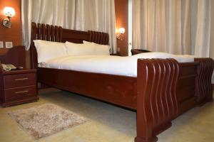 a bedroom with a large wooden bed with white sheets at BWAMI DUBAI HOTEL KASULU 