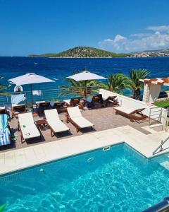 a swimming pool with chairs and umbrellas next to the ocean at Villa Bilic in Rogoznica