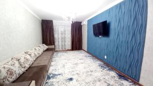 Zimmer mit einem Sofa und einem TV an einer blauen Wand in der Unterkunft 2х комнатная квартира в ЖК Отау сити in Schymkent