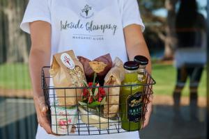 a woman holding a basket of food and drinks at Olio Bello Lakeside Glamping in Cowaramup