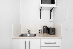 a kitchen with a sink and a microwave at Beach Views on Excellent Studio 27 - Belle Escapes Jervis Bay in Vincentia