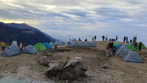 a group of people standing on top of a mountain with tents at Triund Trek and Camping in Dharamshala