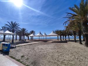 una playa con sombrillas blancas y palmeras en Bonita casa al lado de la playa en Santa Pola, en Santa Pola