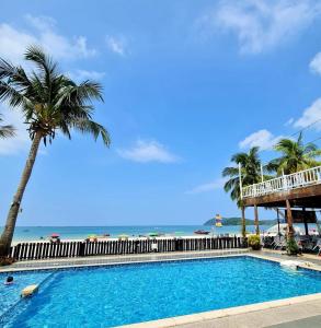 een zwembad naast een strand met een palmboom bij Best Star Resort in Pantai Cenang