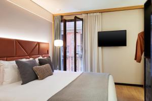 Kimpton Vividora Hotel by IHG في برشلونة: غرفة نوم بها سرير كبير وتلفزيون بشاشة مسطحة