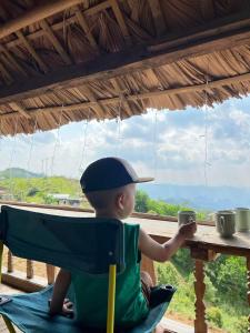 a little boy sitting in a high chair holding a cup at Mường Ecolodge Hòa Bình in Hòa Bình