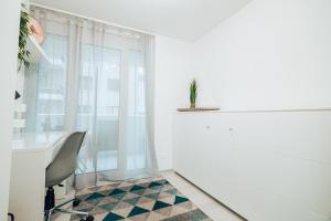 um quarto branco com uma cadeira, uma secretária e uma janela em Central Apartment - culture & nightlife in one em Visp