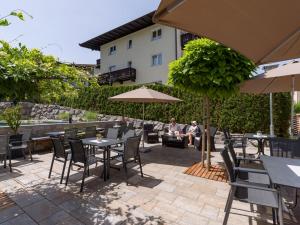 eine Terrasse mit Tischen, Stühlen und einem Sonnenschirm in der Unterkunft Hotel Gänsleit in Söll