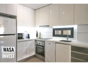 a white kitchen with a sink and a refrigerator at Pinada Beach IV new & comfort. apartment, 1st line to the beach, sunterrace+pool in La Mata