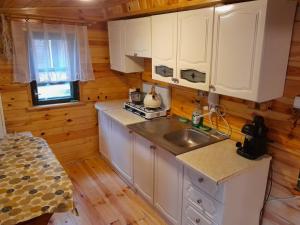 uma cozinha com armários brancos e um lavatório numa cabina em Domek Leśny Klimat em Serpelice