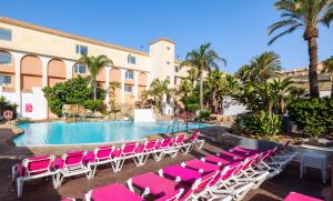 a pool with pink lounge chairs next to a building at Diverhotel Roquetas in Roquetas de Mar
