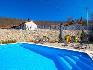 a blue swimming pool with chairs and a stone wall at Villa Lemily in Matulji