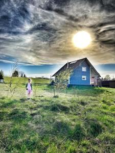 une femme debout dans un champ à côté d'une maison bleue dans l'établissement Czaplowisko - domki z sauną na Kaszubach, à Stare Czaple