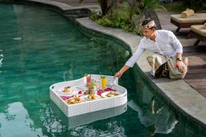 a man sitting next to a pool with a tray of food at Aryaswara Villa Ubud in Ubud +25 photos