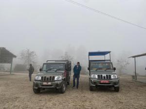 Dos jeeps estacionados en la niebla con un hombre parado entre ellos. en Hotel Shiva's Dream, en Sauraha