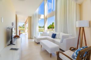 una sala de estar con muebles blancos y ventanas grandes. en Reserva Sauípe - Casa 189 en Costa do Sauipe