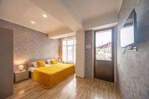 Schlafzimmer mit einem Bett mit gelber Bettwäsche und einem TV in der Unterkunft Tskaltubo Hotel Terrace in Zqaltubo