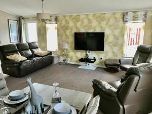 a living room with leather furniture and a flat screen tv at Rannoch Lodge in Auchterarder