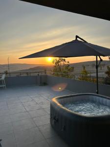a hot tub with an umbrella with the sunset in the background at נס הבריאה in Midreshet Ben Gurion