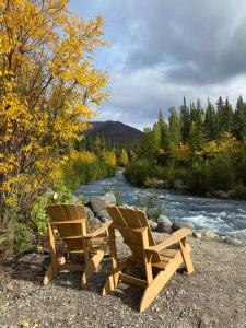 two wooden chairs sitting next to a river at McKinley Creekside Cabins in McKinley Park