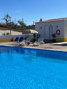 a blue swimming pool with chairs and an umbrella at Hospedaria O Castelo in Portel