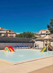 una piscina con sillas y un arco iris en el agua en MobileHome 8 Personnes avec Clim situé au Camping l'Elysée Grau du roi Vagues Océanes By CapFun en Le Grau-du-Roi