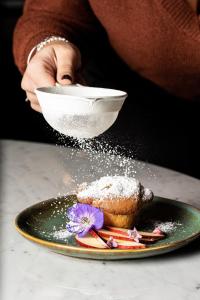 une personne arrosant du sucre en poudre sur une pâtisserie sur une assiette dans l'établissement Hotel Mercure Roma Corso Trieste, à Rome