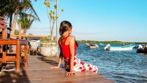 Ein junges Mädchen sitzt auf einem Dock in der Nähe des Wassers in der Unterkunft Hotel Restaurante Spa La Barca de Oro in Las Peñitas