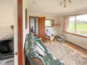 a living room with a green leather couch and a window at Gean Cottage in Powmill