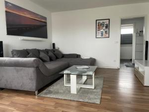 a living room with a gray couch and a glass table at FeWo an der Nordseeküste mit Garage in Wilhelmshaven