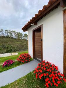 a white building with red flowers and a door at Chalé Lírio do Campo in Ouro Preto