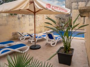 un patio con sillas, una sombrilla y una piscina en Sunny Villa en Nadur