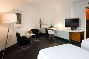 a room with a desk and a tv and chairs at Dorint Kongresshotel Düsseldorf/Neuss in Neuss