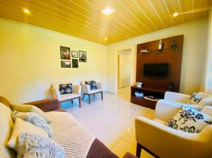 ein Wohnzimmer mit einem Bett, Stühlen und einem TV in der Unterkunft Casa ampla e aconchegante em Gramado in Gramado