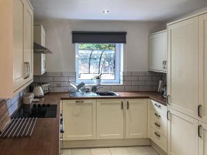 uma cozinha com armários brancos, um lavatório e uma janela em Clock Tower Cottage em Whitchurch