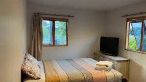 a bedroom with a bed and a tv and two windows at Visitor Rooms Prepay & Self Check in in Queenstown