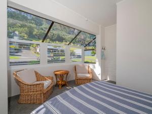 a bedroom with a bed and chairs and a large window at Opito Sea'scape - Opito Bay Holiday Home in Opito Bay