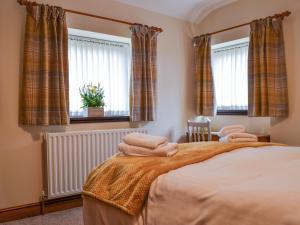 a bedroom with a bed with two windows and towels at Scalelands Cottage in Frizington