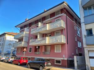 un edificio rosa con macchine parcheggiate di fronte di Cardellino, piccolo e accogliente dietro la spiaggia a Grado