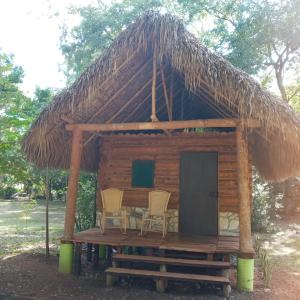 a cabin with two chairs and a thatched roof at Room in Cabin - Cabins Sierraverde Huasteca Potosina Green Cabin in Damían Carmona