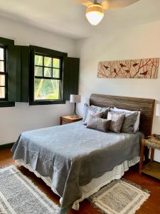 a bedroom with a bed with a blue comforter and two windows at Chalés Cores da Mata in Tiradentes