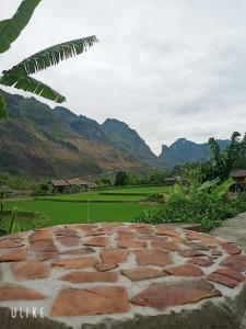 a stone patio with a green field and mountains in the background at Du Già Vân Chung Homestay in Làng Cac