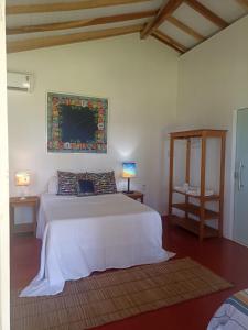 a bedroom with a white bed and a painting on the wall at Pousada Flor de Elisa frente a praia in Caraíva